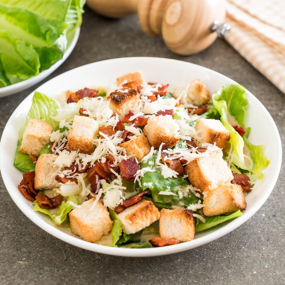 A Caesar salad with crisp romaine lettuce, crunchy croutons, bacon bits, and shredded Parmesan cheese.