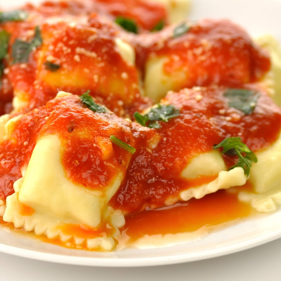 Close-up of Florina's ravioli pasta covered in red tomato sauce and green herbs.