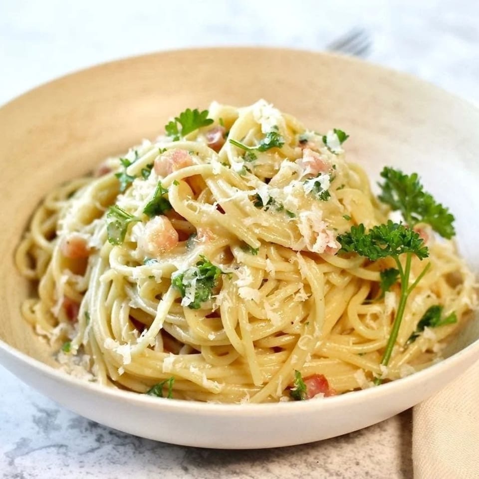 A bowl of spaghetti carbonara, topped with grated cheese, bacon bits, and fresh parsley.